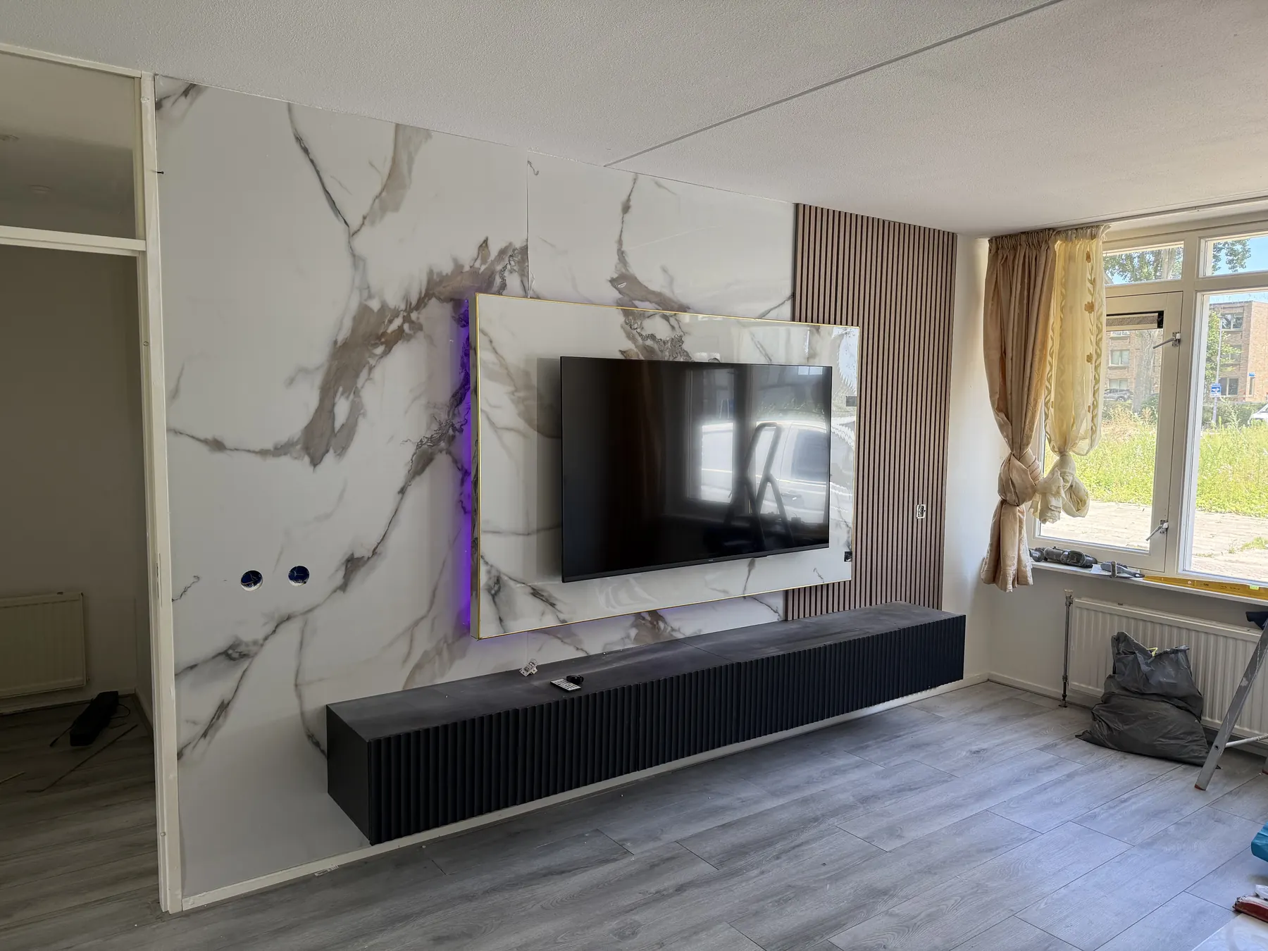 Elegante cinewall met wit marmeren achterwand, zwarte zwevende kasten en sfeerverlichting